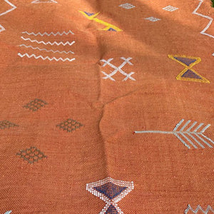 Close-up of a handwoven terracotta Moroccan runner rug with intricate Berber symbols and arrow motifs in white, yellow, and blue on grass