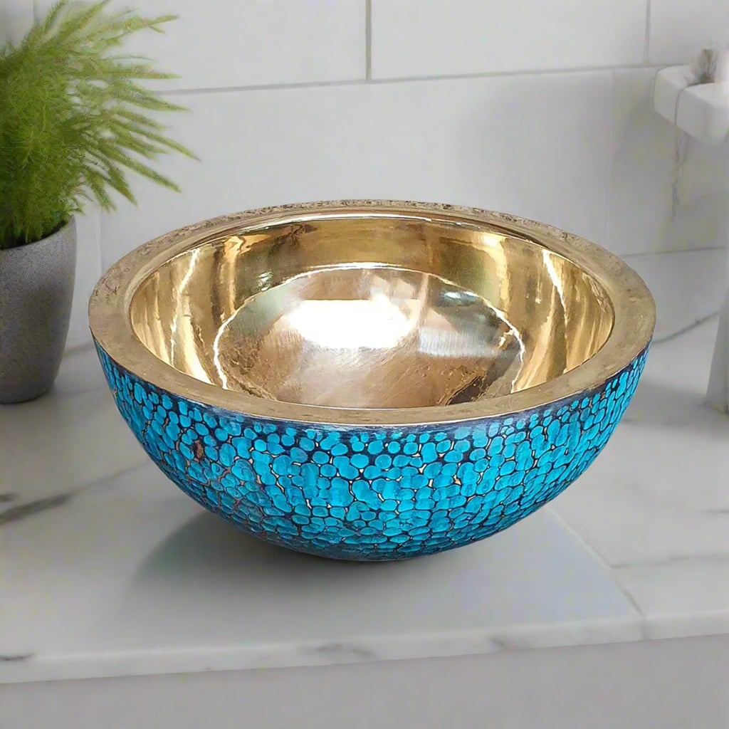 Round brass bathroom basin with a textured turquoise exterior and reflective golden interior on a white marble surface