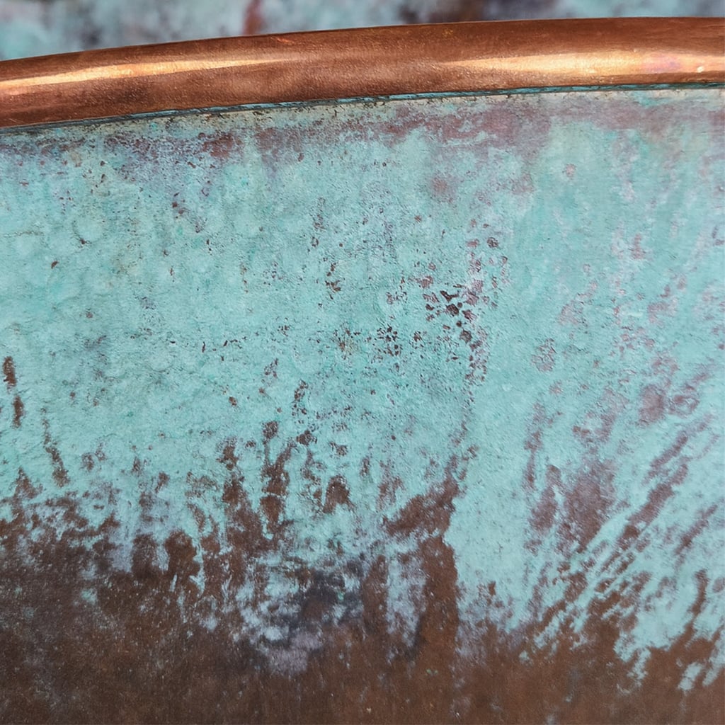 Close-up of hammered copper sink with natural verdigris patina finish, highlighting artisan texture and aged green-blue tones