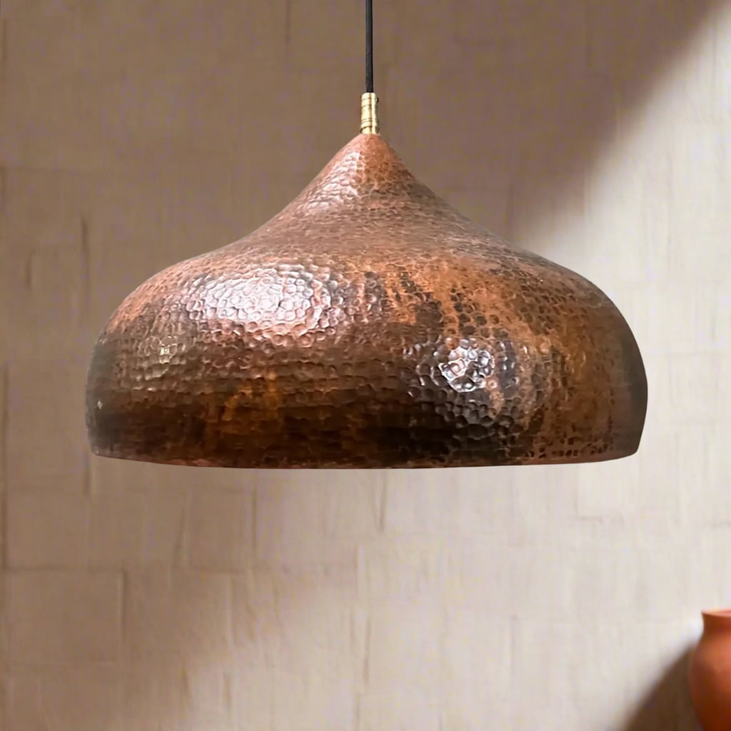 Curved copper dome light with a hammered texture, suspended against a neutral wall with soft ambient lighting