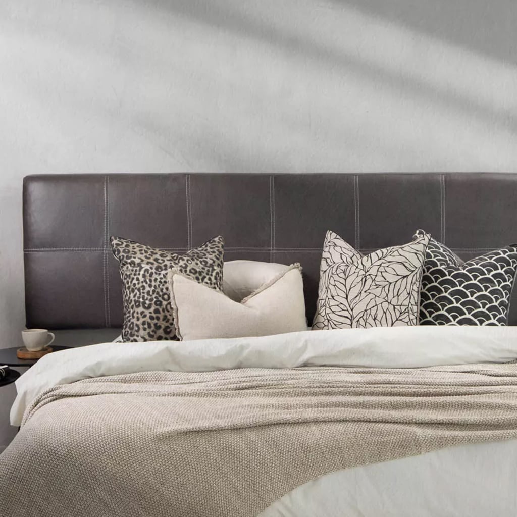 A modern bedroom featuring a black leather headboard with white contrast stitching, styled with a mix of neutral and patterned throw pillows