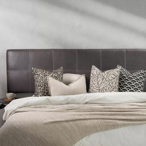 A modern bedroom featuring a black leather headboard with white contrast stitching, styled with a mix of neutral and patterned throw pillows