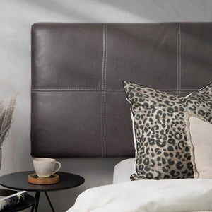 Close-up view of the left side of a black leather headboard with visible stitching detail, next to a nightstand with a cup and decor