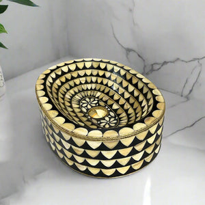 Top corner view of an oval inlay sink with floral center design and brass detailing