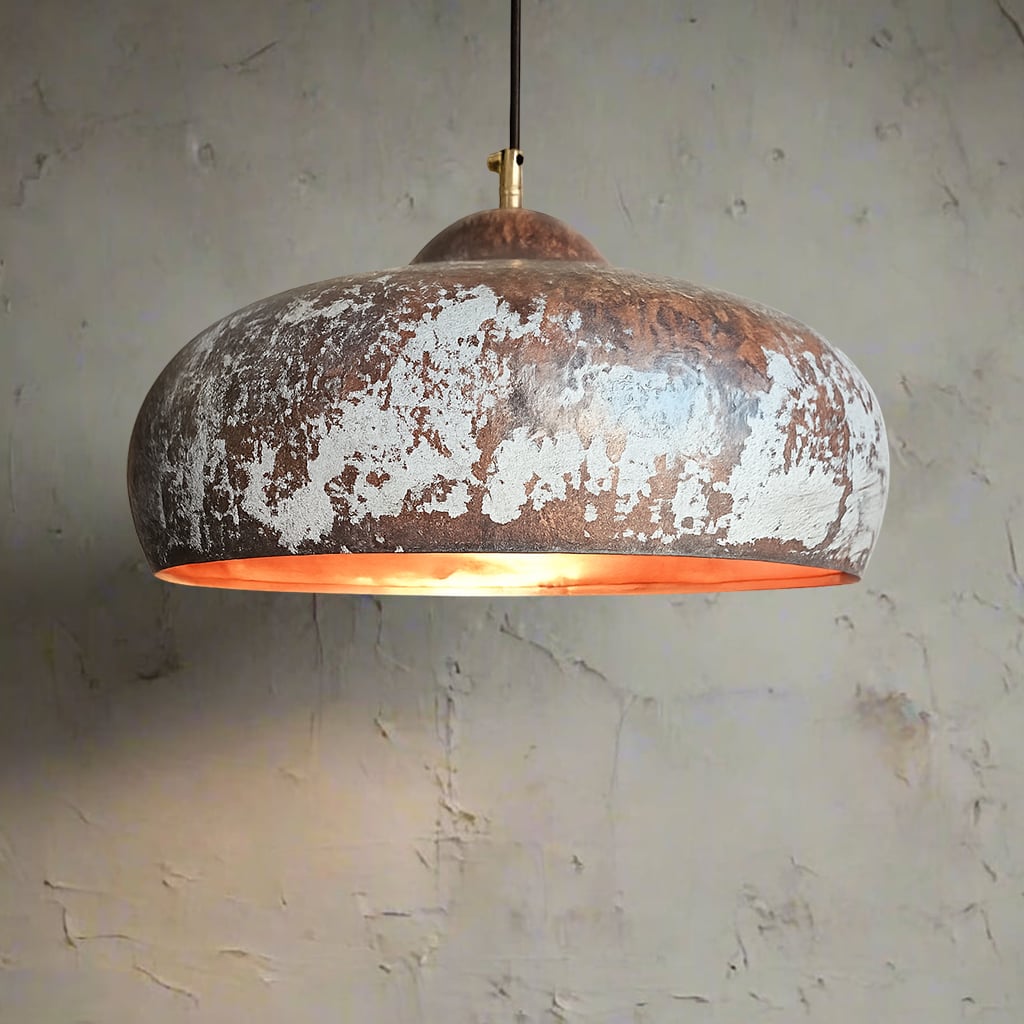 Close-up of a dome-shaped pendant light with a distressed white and copper finish, hanging against a textured wall