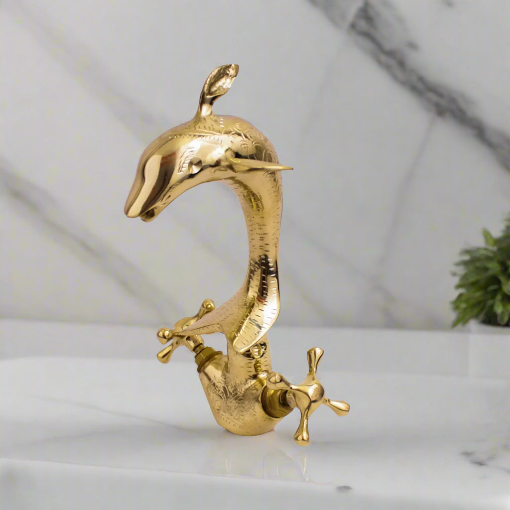 Dolphin-shaped brass faucet with antique engraved finish on marble background