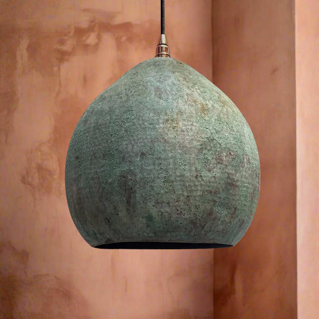 Matte interior dome pendant light with a weathered green patina surface and smooth silhouette, hanging against a textured peach-toned wall
