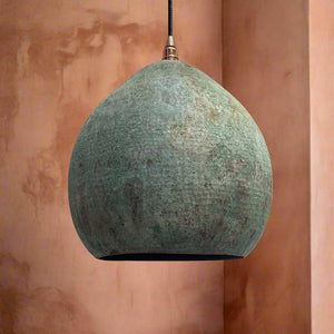 Matte interior dome pendant light with a weathered green patina surface and smooth silhouette, hanging against a textured peach-toned wall
