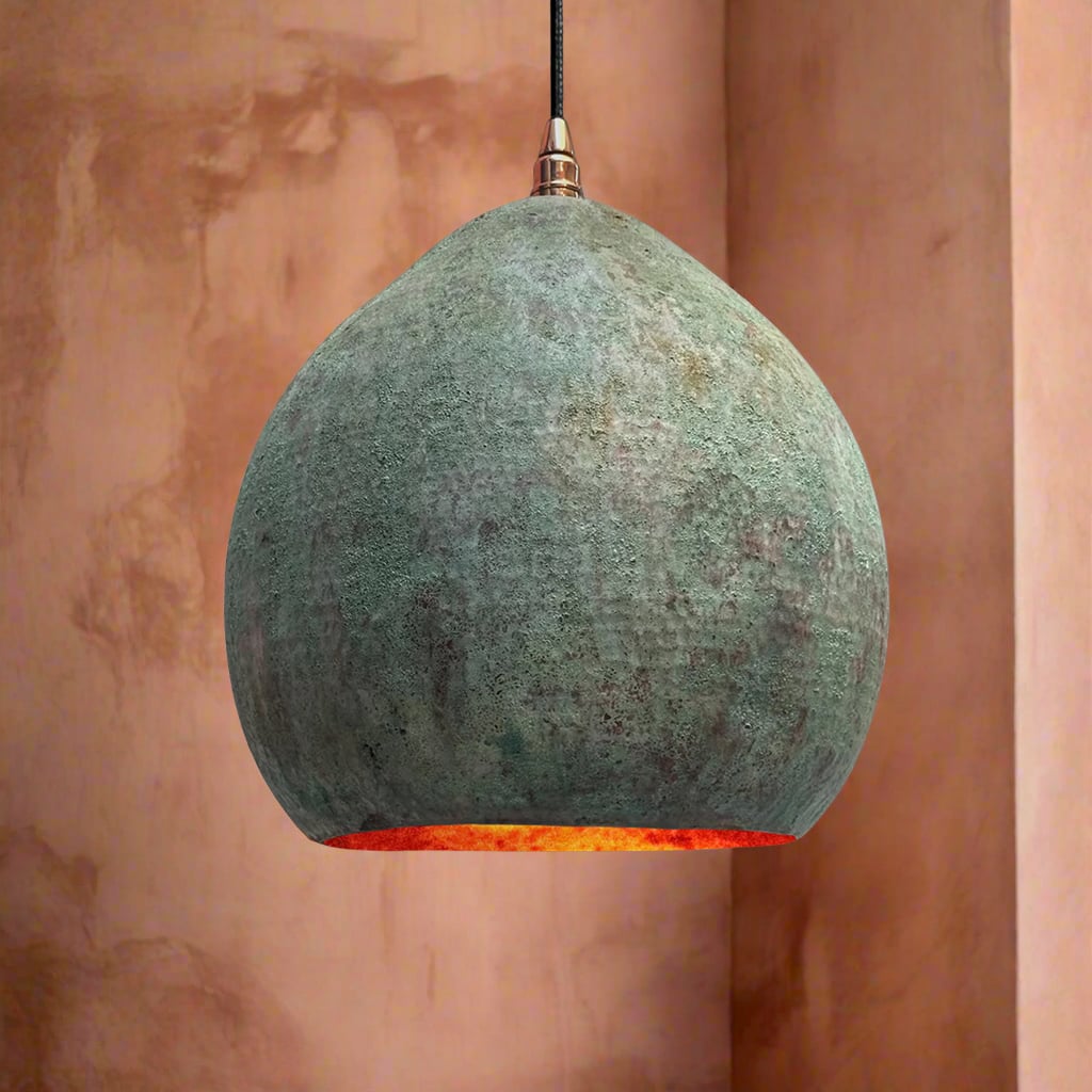Handcrafted dome pendant light with a green patina finish and warm copper interior, hanging in a softly lit, earthy-toned room