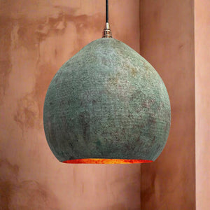 Handcrafted dome pendant light with a green patina finish and warm copper interior, hanging in a softly lit, earthy-toned room