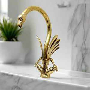 Ornate brass faucet shaped like a swan with feather details and engraved surface, installed on a marble sink for a refined vintage look