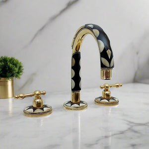 Elegant three-hole bathroom faucet with black and gold finish, decorative inlay, and golden lever handles, styled in a modern bathroom setting
