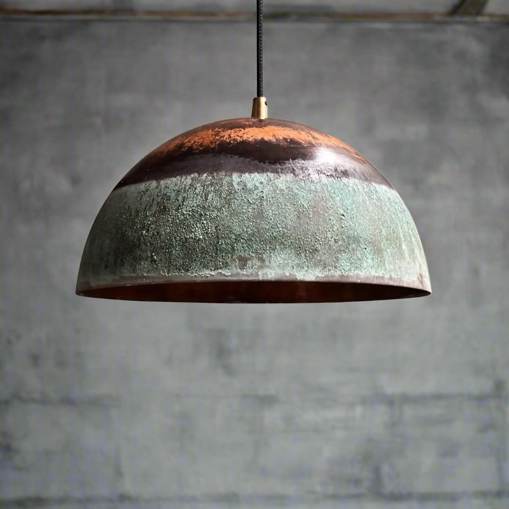 Artisanal green patina and copper pendant light hanging near a window, casting warm ambient light in a textured setting