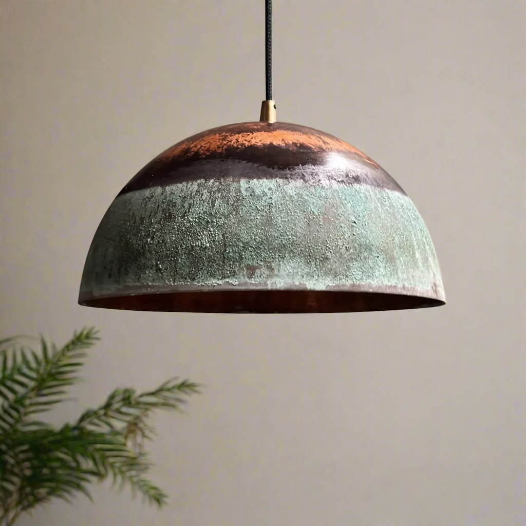 Dome-shaped pendant light with green patina and copper tones, hanging in a softly lit room with neutral tones and a touch of greenery