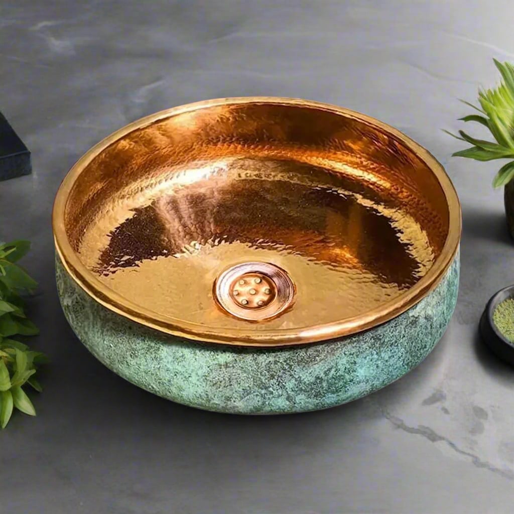 Interior view of a copper wash basin with a green patina exterior and polished copper interior, styled with greenery