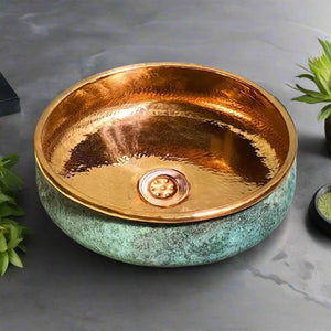 Interior view of a copper wash basin with a green patina exterior and polished copper interior, styled with greenery