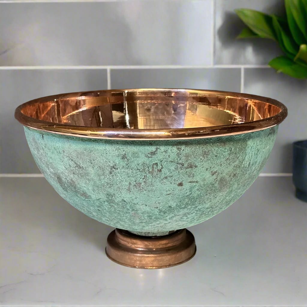 Round green patina copper bathroom sink with polished interior on a light gray countertop
