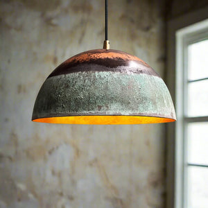 Side profile of green patina dome pendant light with raw copper top, suspended in a moody interior space