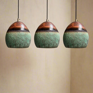 Set of three rounded copper pendant lights with a green patina and oxidized gradient finish, suspended against a neutral wall