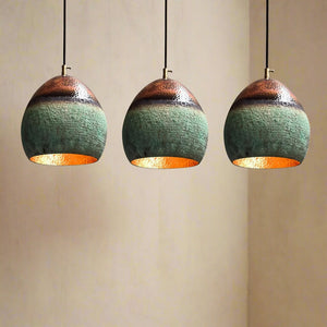 Three hammered copper pendant lights with green patina finish hanging in a row against a warm beige wall.