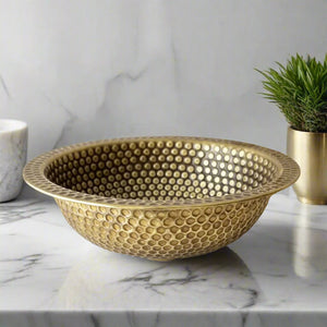 Side angle of a hammered brass drop-in bathroom sink showing elegant texture and shine on a marble vanity