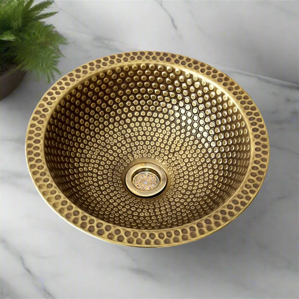 Top view of a hammered brass drop-in bathroom sink with textured circular patterns on a marble countertop