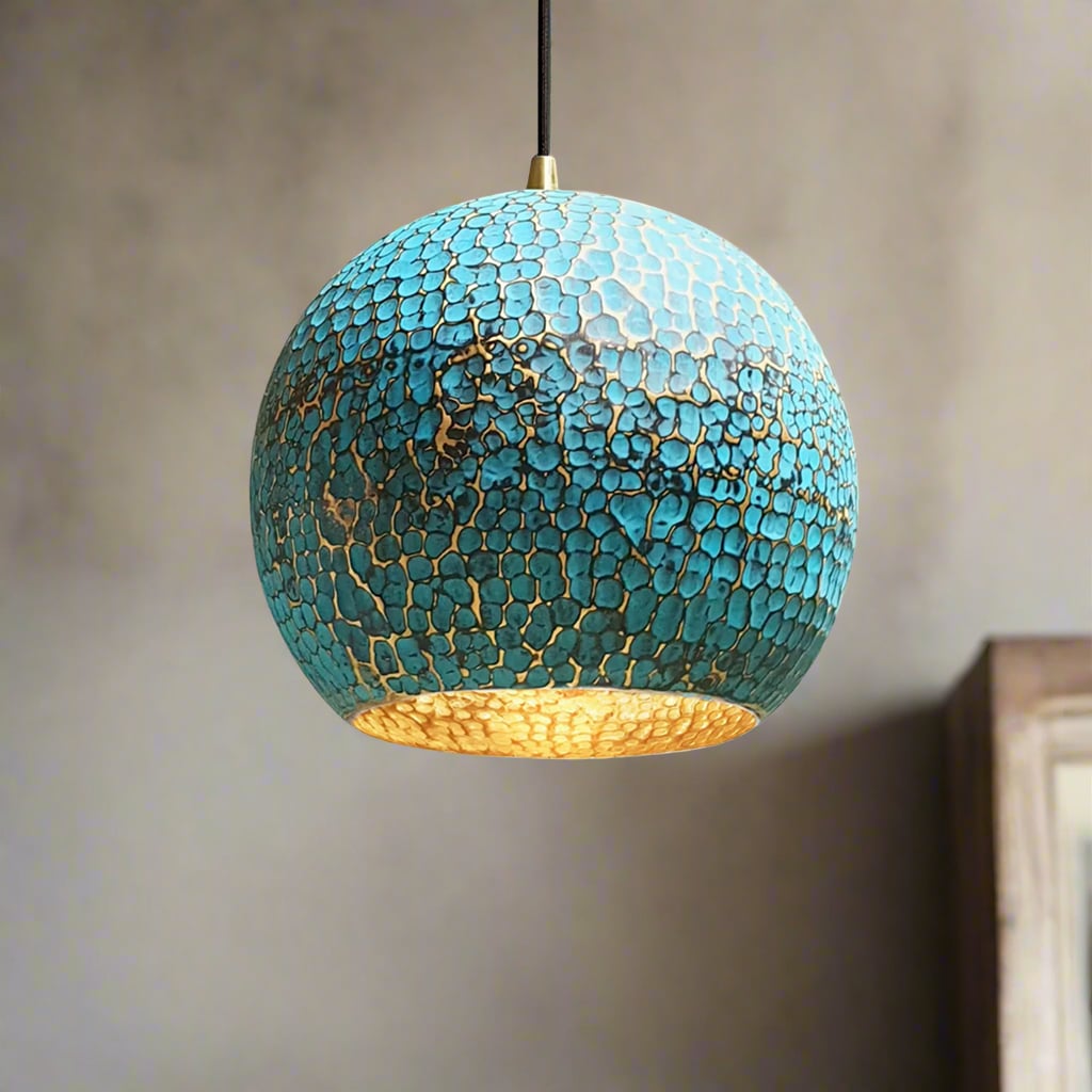 Handcrafted hammered brass pendant light with blue patina finish in a globe shape, casting a warm glow in a softly lit interior