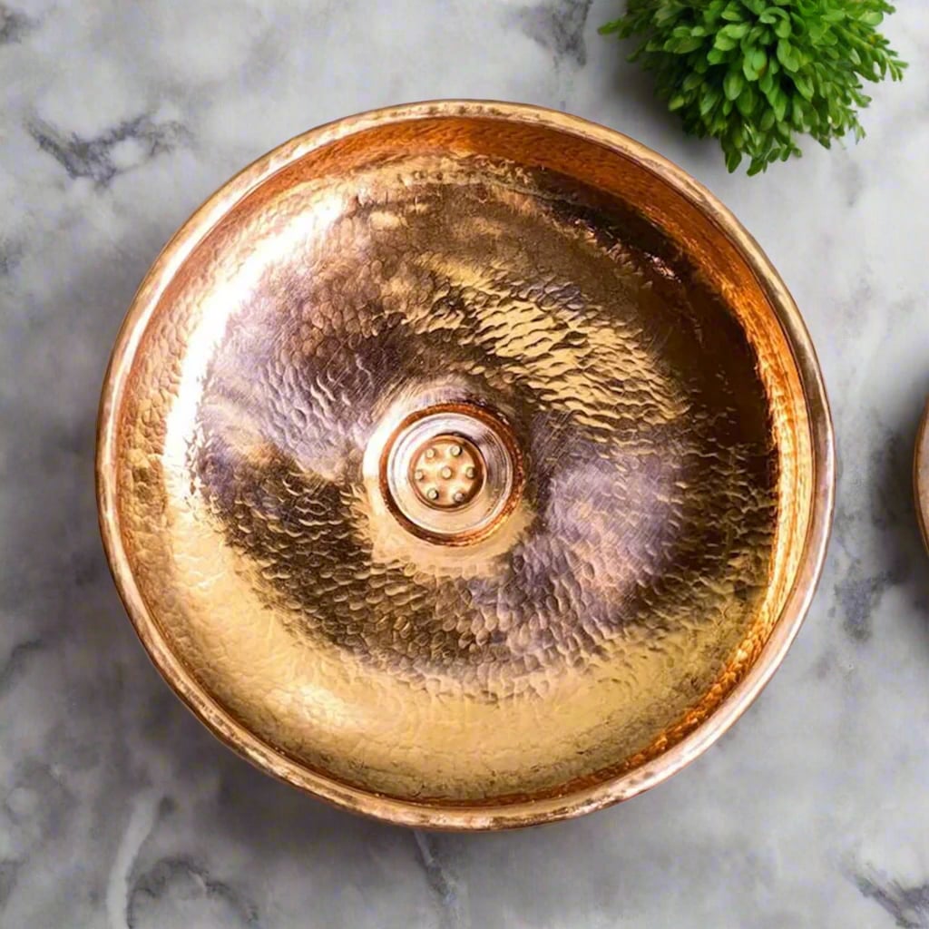 Top view of a handcrafted hammered copper basin with a polished finish, placed on a marble countertop