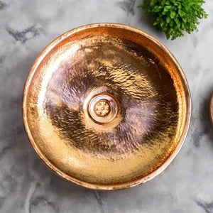 Top view of a handcrafted hammered copper basin with a polished finish, placed on a marble countertop