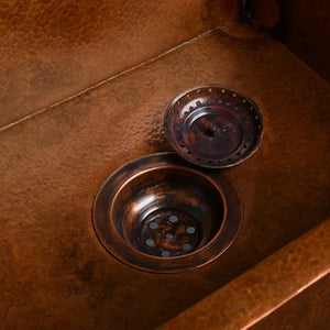 Close-up of a hammered copper kitchen sink with a matching copper drain and strainer