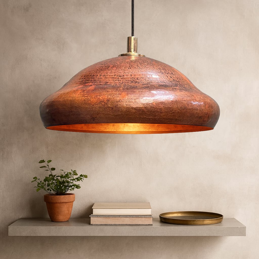 Hand-hammered Moroccan pendant light with a warm copper finish and brass fitting, casting a golden glow onto a neutral-toned interior.