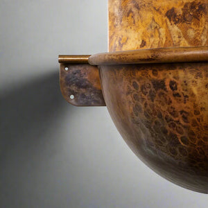 Close-up of a hammered copper wall-hung sink in golden-brown patina, showing detailed texture and sturdy wall-mount bracket