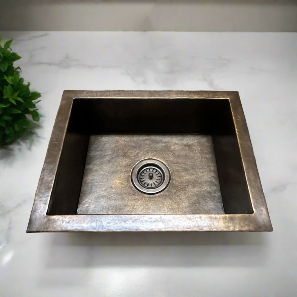 Rectangular hammered nickel kitchen sink with clean edges, shown installed in a white marble countertop with a green plant nearby