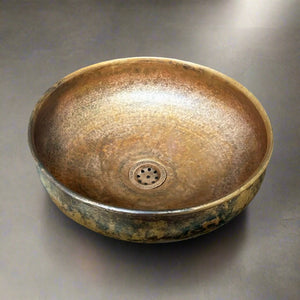 Hammered patina copper basin sink with a rustic finish and integrated drain, shown on a dark countertop