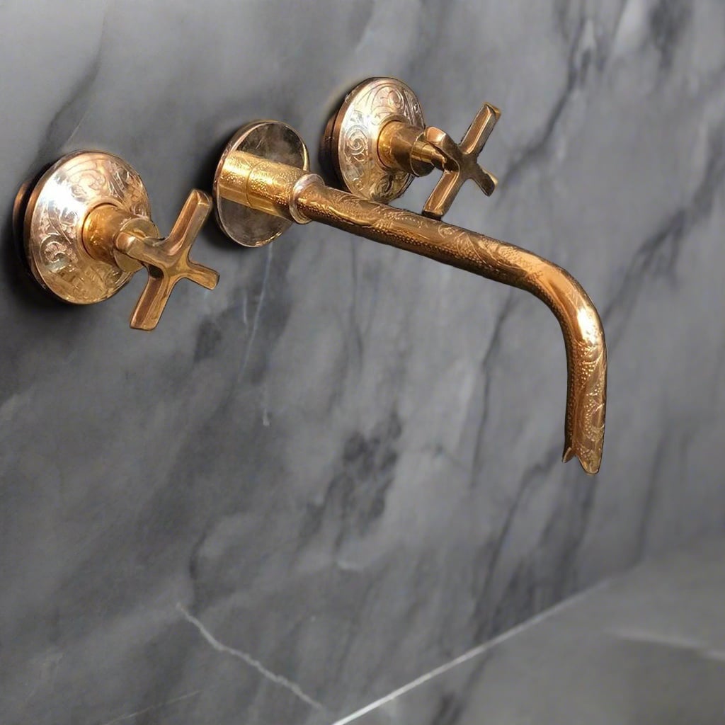 Unlacquered brass gooseneck wall faucet with cross handles mounted on a marble bathroom wall