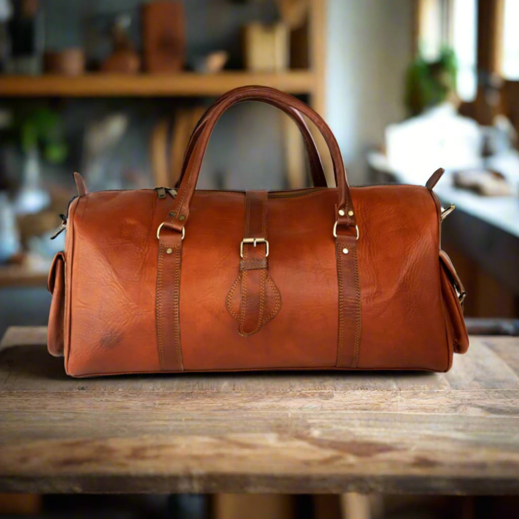 A front view of a handcrafted leather travel duffle bag in a warm reddish-brown tone. The bag features reinforced handles, sleek stitching, and a classic buckle detail, perfect for stylish and practical travel