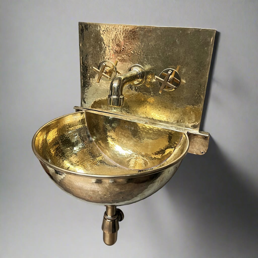 A commercial packshot of a handcrafted wall-hung hammered brass sink with golden finish, featuring brass faucet and cross handles