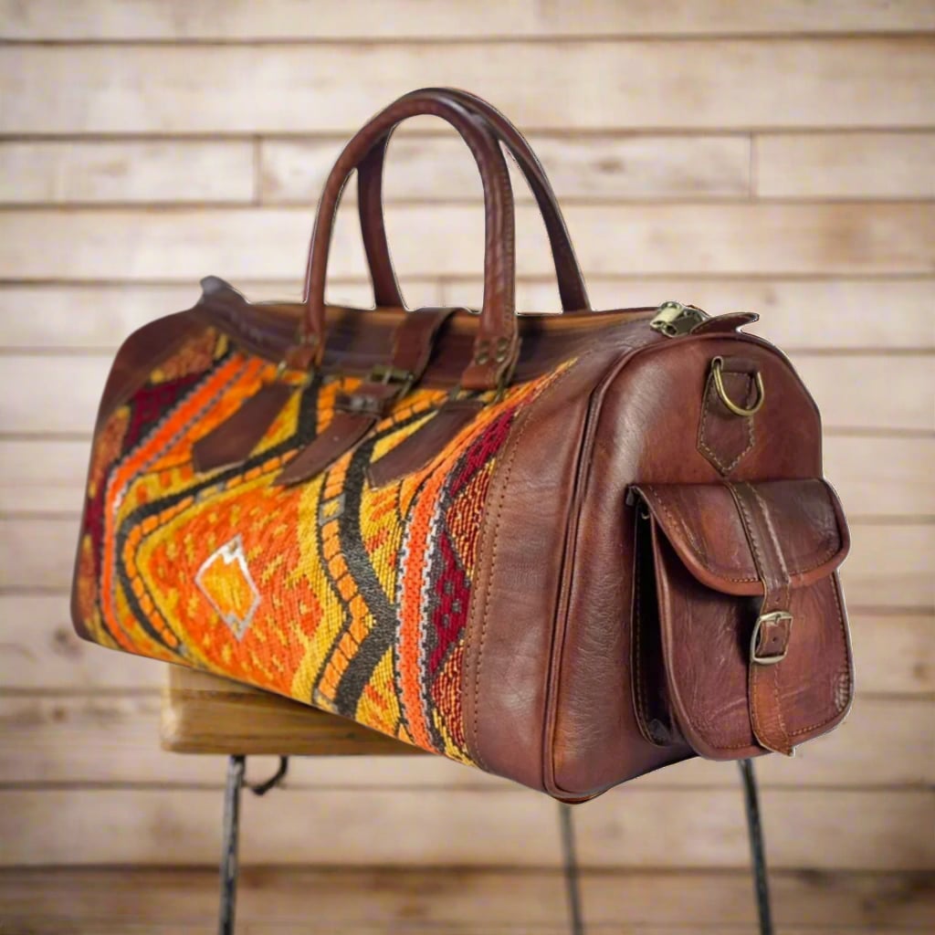 A handcrafted travel bag made with premium brown leather and vibrant kilim accents in warm orange, red, and yellow tones. Features a side pocket and sturdy handles