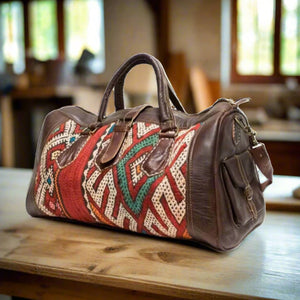 A handcrafted Moroccan travel bag made with premium brown leather and vibrant kilim accents featuring red, green, and white geometric patterns