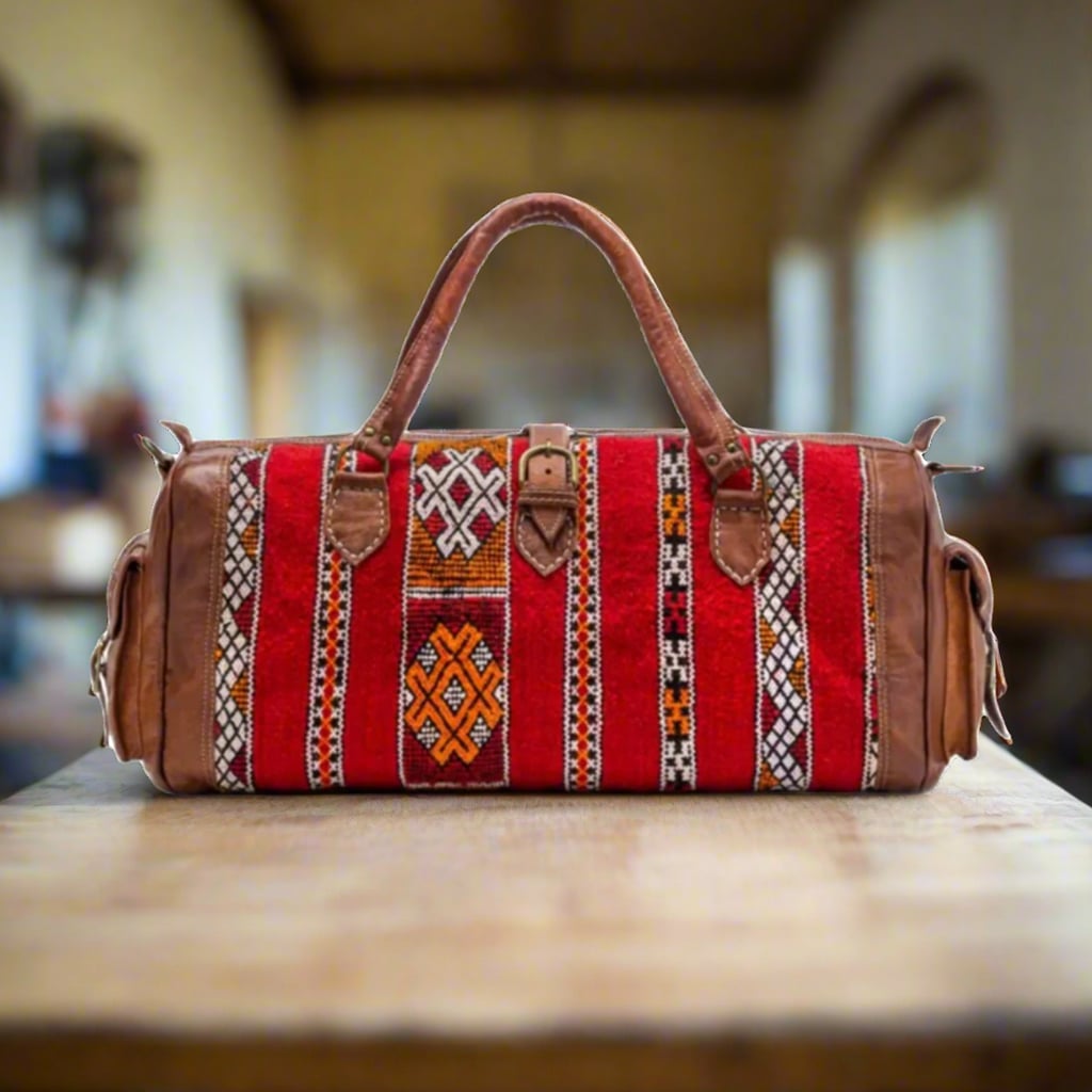 A front view of a handcrafted Moroccan travel bag made with premium leather and vibrant red kilim accents featuring bold striped patterns and intricate geometric designs