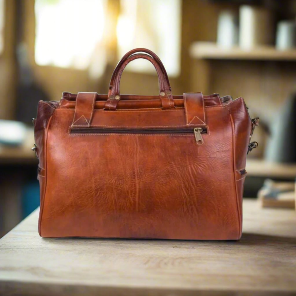 A back view of a handcrafted leather weekend bag in a rich reddish-brown tone, featuring a zippered pocket for secure storage and sturdy leather handles.