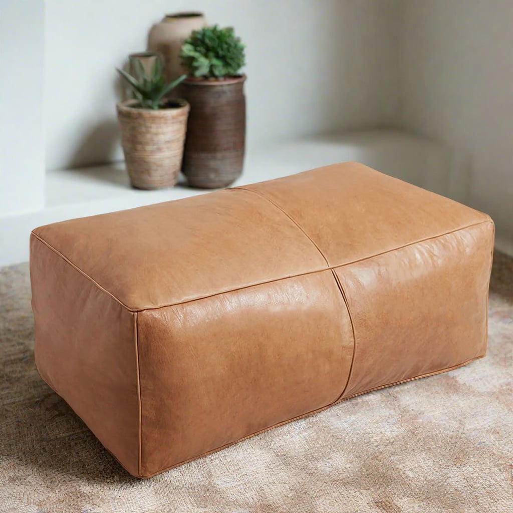 Handcrafted rectangular tan leather ottoman placed in a modern living room featuring natural decor elements such as potted plants and woven baskets, set against a neutral color scheme.