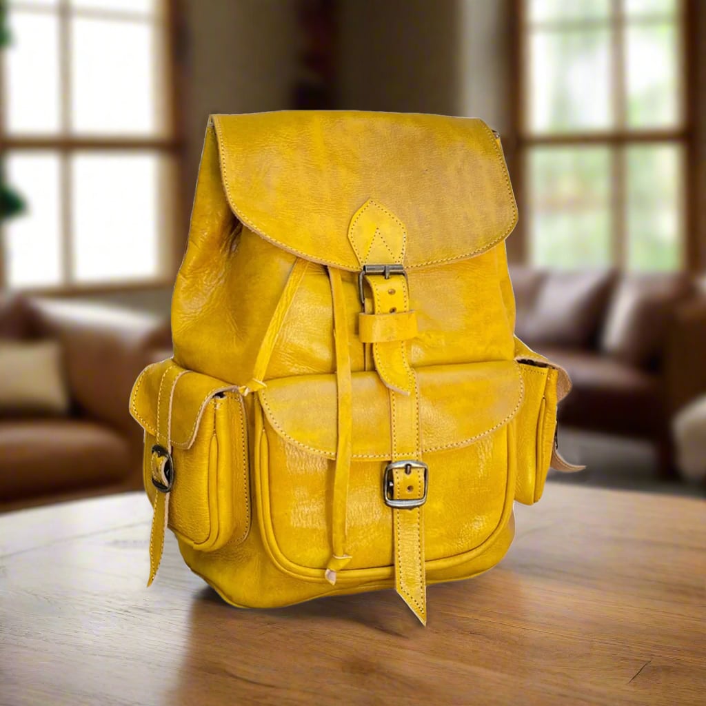 Bright yellow Moroccan leather backpack featuring buckle closures and side pockets, displayed on a wooden table with a leather sofa and large windows in the background