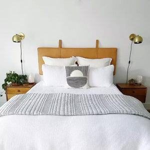 Scandinavian-style white bedroom with queen-size bed, light sheets, pillows, hanging brass reading lamps, leather headboard - Moroccan Interior