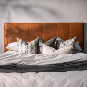Front view of a Patterned white, brown, & black pillows on the bed with white linen, and a dark tan leather headboard - Moroccan Interior.