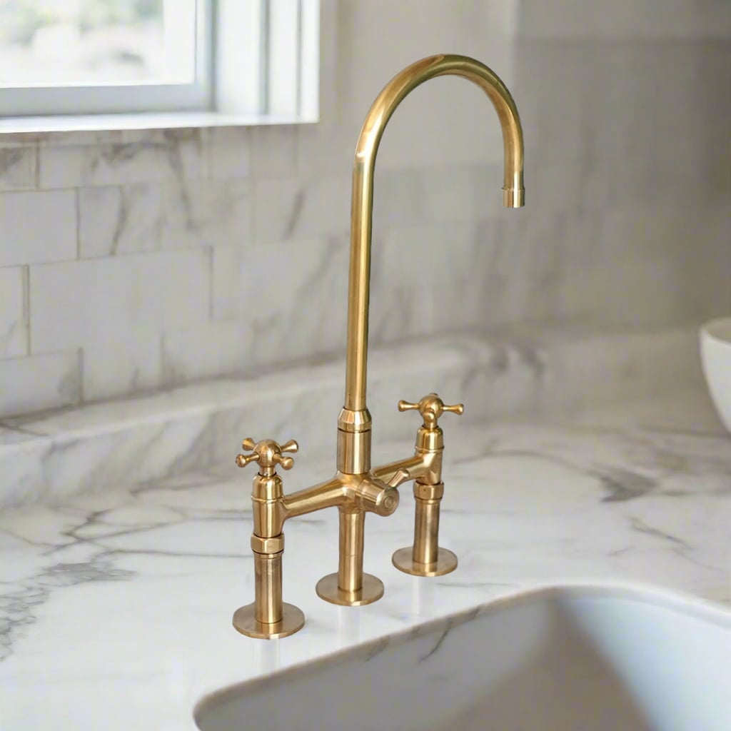 Tall gooseneck brass faucet with classic cross handles on a sleek marble kitchen worktop, positioned beside an under-mount sink and window