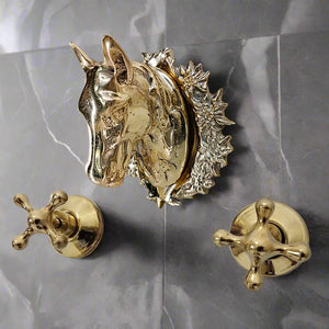 Close-up of a brass wall-mounted faucet set featuring a sculpted horse head spout with detailed mane, mounted on a dark marble wall with gold cross-handle knobs