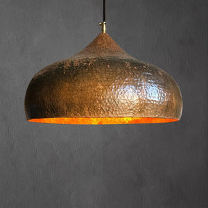 Illuminated hammered copper pendant lamp glowing warmly from underneath, highlighting the rich copper tones and dome silhouette