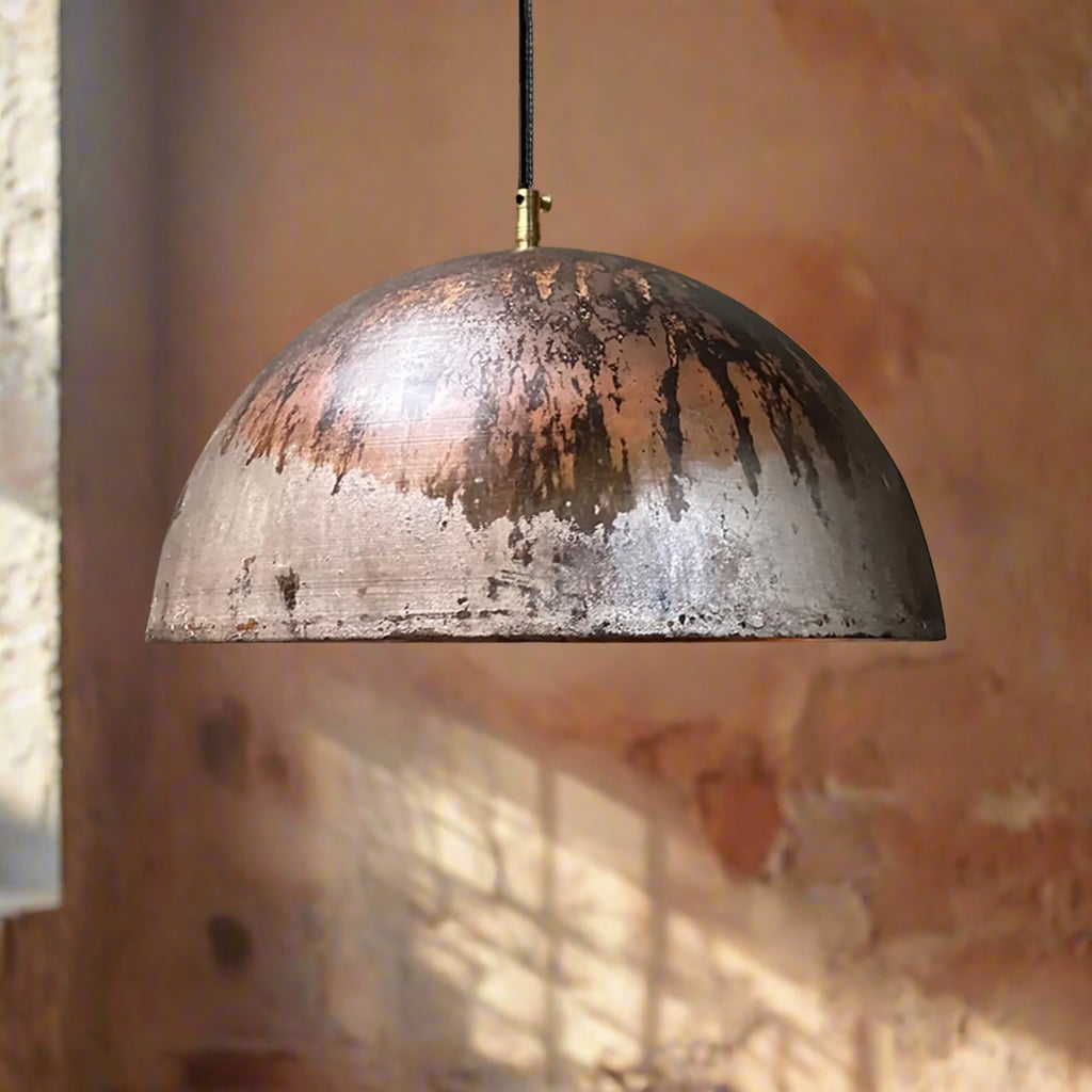 Industrial-style copper dome pendant light featuring a raw oxidized patina finish, hanging in front of a softly lit rustic wall