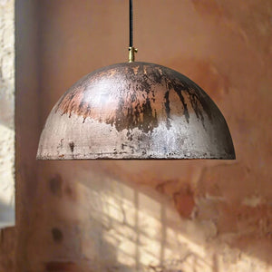 Industrial-style copper dome pendant light featuring a raw oxidized patina finish, hanging in front of a softly lit rustic wall